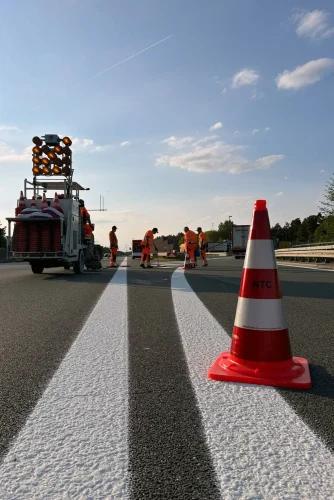 Ein Verkehrsleitkegel mit Beschriftung NTC auf einer frisch markierten Straße.